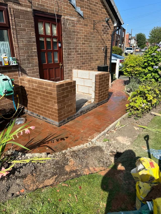 Front boundary wall under construction in buff facing brick, with new block paving outside a bungalow