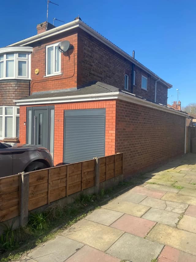 Red-brick garage extension with grey roller door added to a 1930s bay-fronted semi-detached house