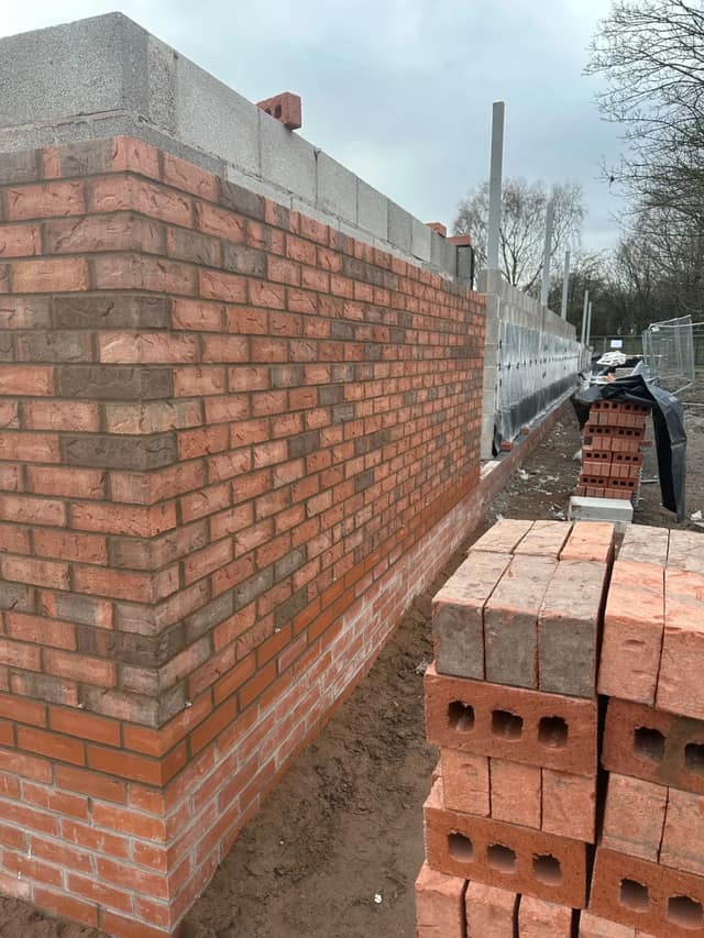 Facing brickwork rising at a corner, block backing above and packs of bricks staged for the next lift