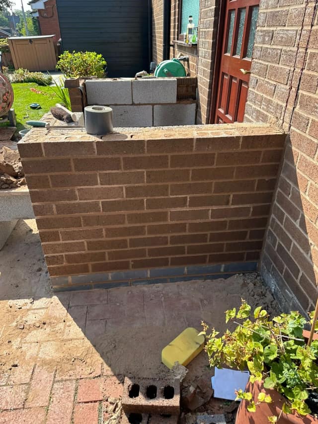 New brick store walls rising off a fresh damp-proof course beside the back door of a brick semi